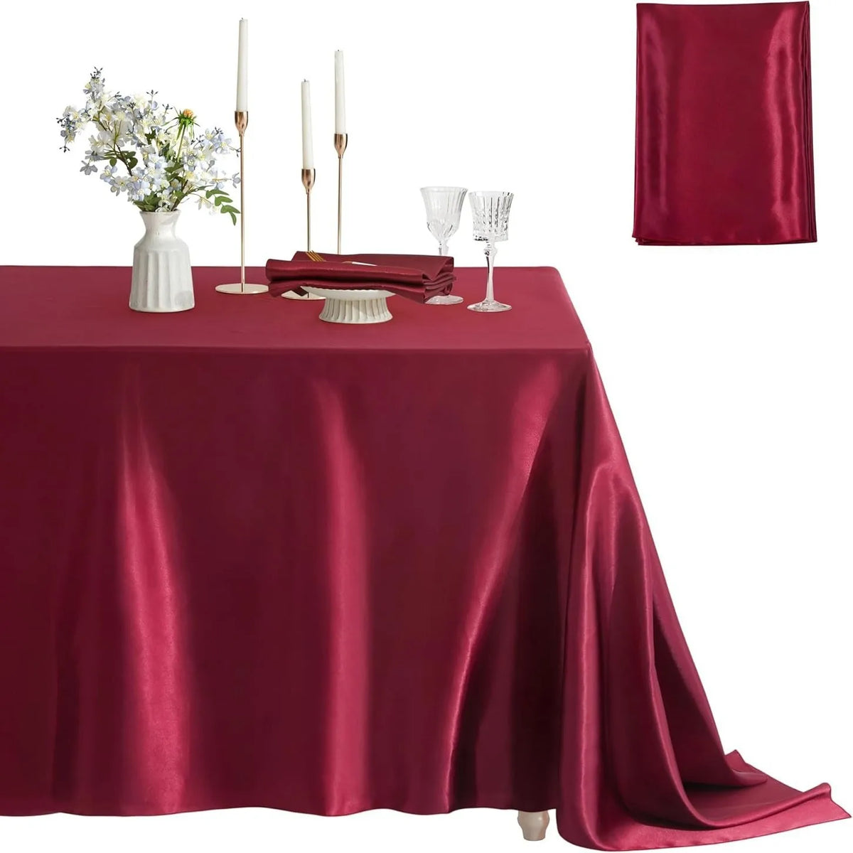 A deep red satin tablecloth set for elegant dining featuring a floral centerpiece, candles, and glassware.