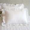 A white soft cotton ruffle pillow cover with delicate frills resting on a white bed.