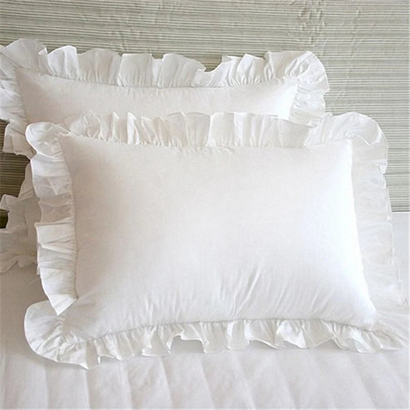A white soft cotton ruffle pillow cover with delicate frills resting on a white bed.