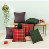 A set of two red and green tartan plaid decorative throw pillow covers displayed on a wooden bench against a light green wall