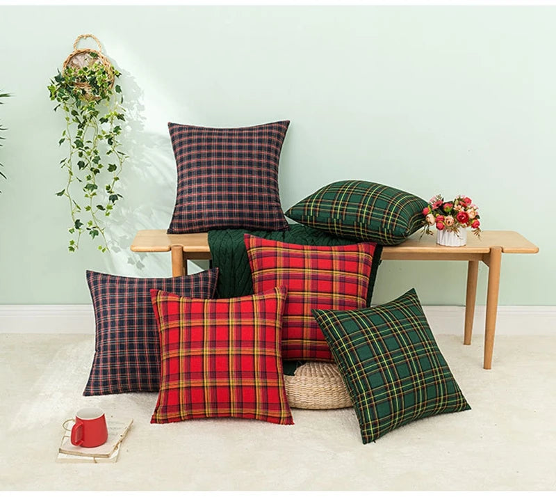 A set of two red and green tartan plaid decorative throw pillow covers displayed on a wooden bench against a light green wall