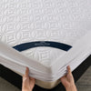 A white quilted mattress protector with a navy blue band is being held by hands.