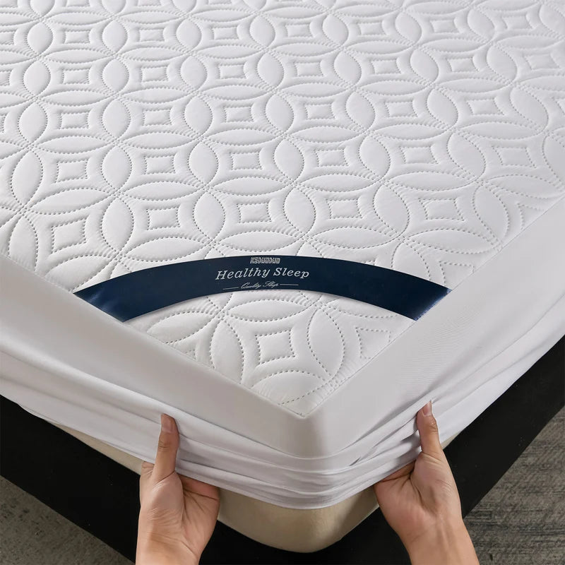 A white quilted mattress protector with a navy blue band is being held by hands.