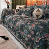 A dark floral jacquard sofa throw blanket draped over a sofa with patterned pillows and warm lighting.