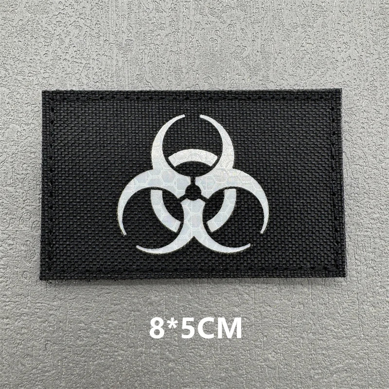 A black embroidered patch featuring a white biohazard symbol on a gray background.