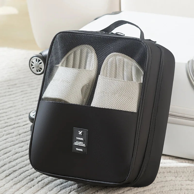 A black portable travel shoe organizer bag with two mesh compartments is shown on a light surface.