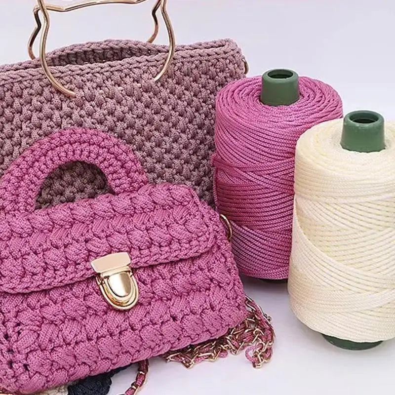 A pink crocheted handbag next to spools of purple and cream ice rope yarn for crafting.
