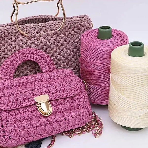 A pink crocheted handbag next to spools of purple and cream ice rope yarn for crafting.