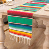 Colorful cotton Mexican sarape table runner with multicolored stripes and fringe on a wooden table.