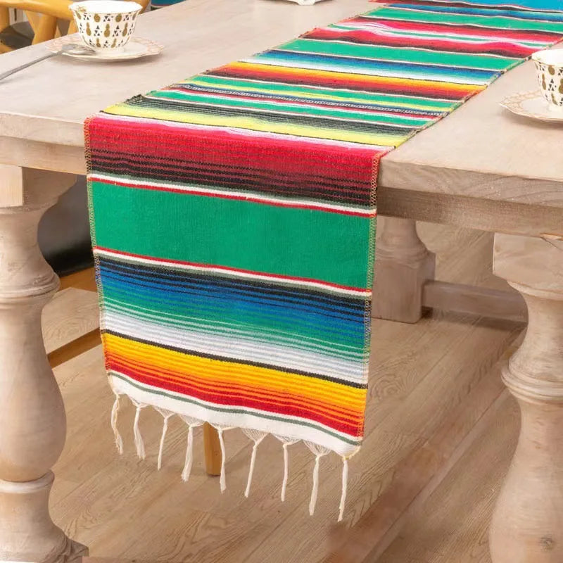 Colorful cotton Mexican sarape table runner with multicolored stripes and fringe on a wooden table.
