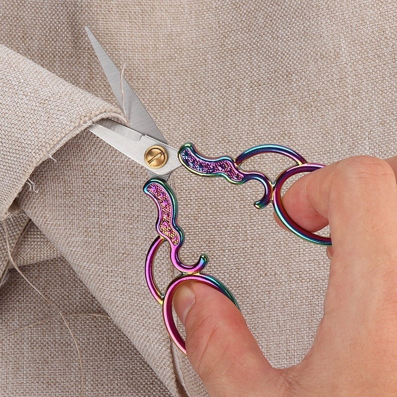 A hand is using vintage stainless steel sewing scissors to cut fabric on a light beige garment.