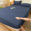 A dark blue fitted bed sheet is draped over a wooden bed frame, with a hand adjusting the fabric.