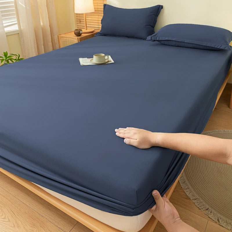 A dark blue fitted bed sheet is draped over a wooden bed frame, with a hand adjusting the fabric.