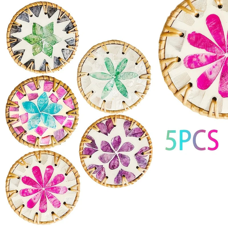 A set of five decorative woven shell coasters featuring floral patterns in various shades of green, pink, and purple.