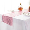 A pink sequin table runner is laid on a white tablecloth with a bottle of amber liquid and silverware.