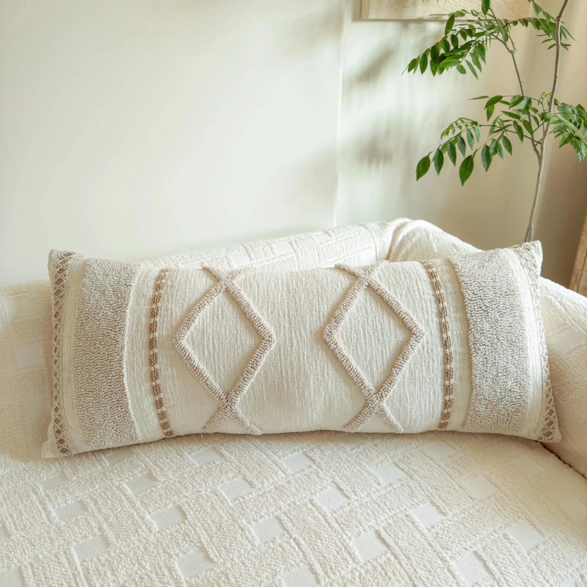 A close-up of a cream knit pillow cover with diamond stitching resting on a white sofa.