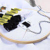 A set of white and black embroidery floss threads with various colors and a needle displayed on a wooden circle.