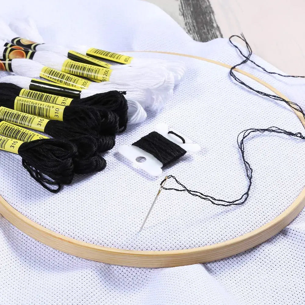 A set of white and black embroidery floss threads with various colors and a needle displayed on a wooden circle.