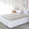 A white bed with an elegant elastic skirt and white bedding set in a bright room.