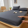 A dark gray fitted sheet is draped over a wooden bed frame, showing its deep pockets and elastic edges.