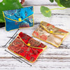 Two silk brocade jewelry pouches in blue and red floral patterns are displayed on a white wooden surface.