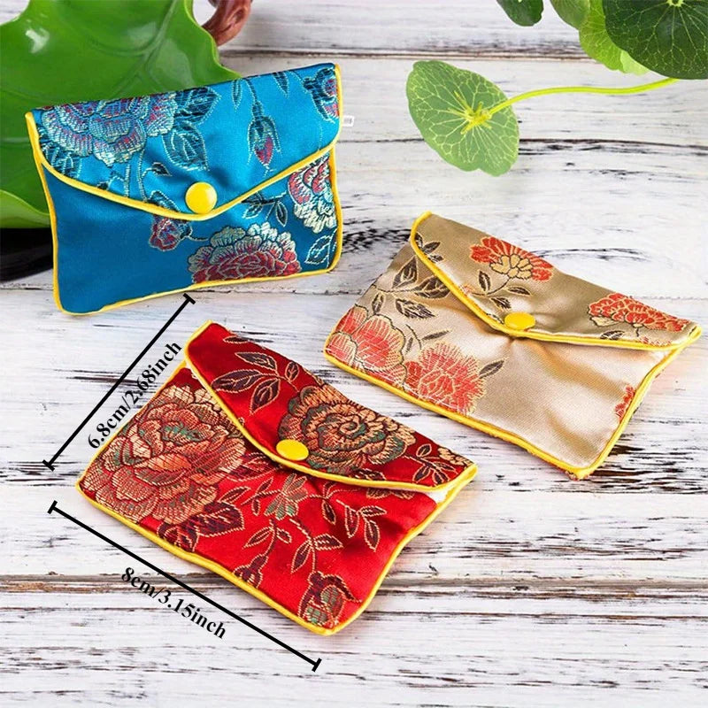 Two silk brocade jewelry pouches in blue and red floral patterns are displayed on a white wooden surface.