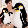 A woman is sitting next to a large black and white penguin plush toy.