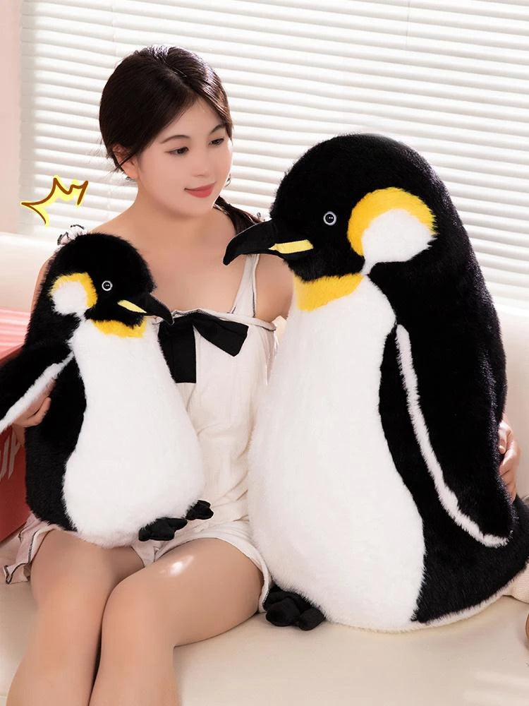 A woman is sitting next to a large black and white penguin plush toy.