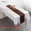 A dark brown satin table runner is displayed on a white tablecloth set for a formal dining arrangement.