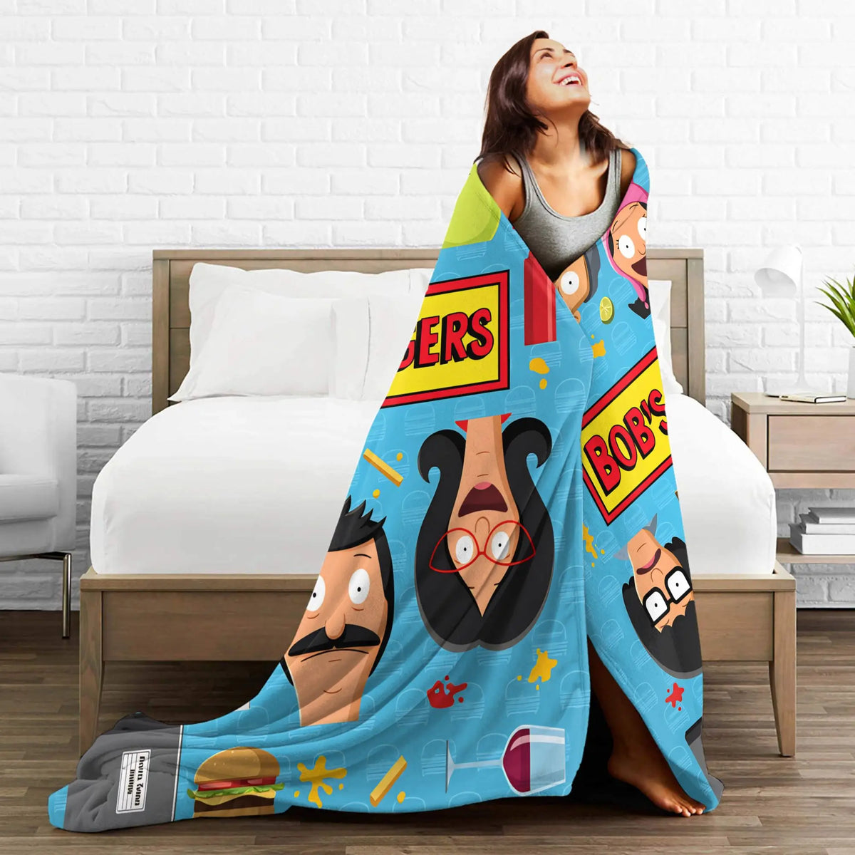 A woman is relaxing on a bed with a colorful throw blanket featuring cartoon characters and text.