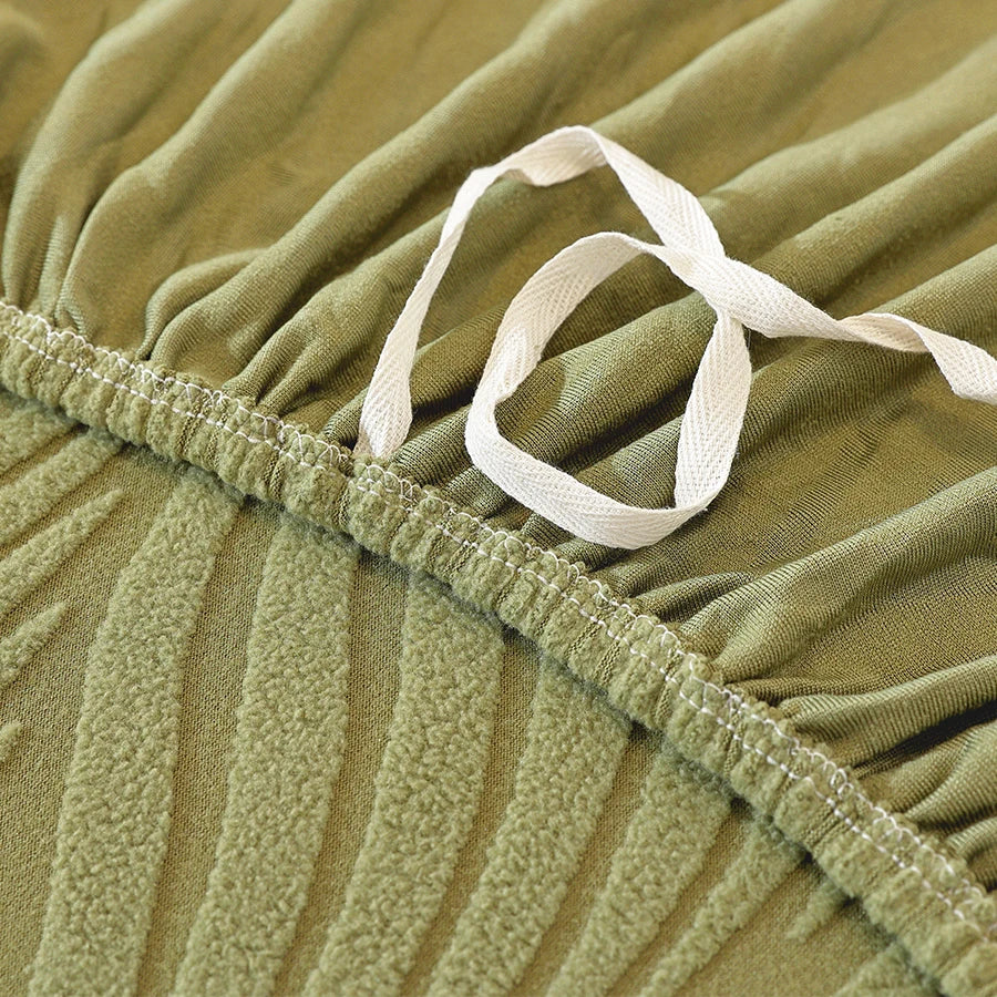 Close-up of a olive green stretch sofa cover with vertical stripes and a white elastic edge detail.