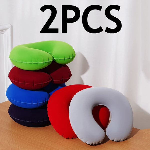 Two green, red, blue, and white inflatable U-shaped travel pillows are displayed on a wooden surface.
