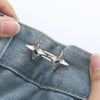 A close-up of a silver star-shaped adjustable waist tightening buckle attached to denim fabric.