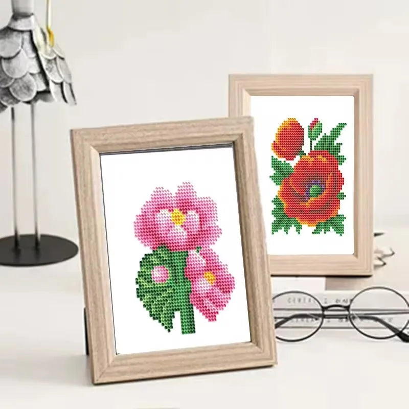 A framed diamond painting featuring a pink flower surrounded by green leaves and red petals.