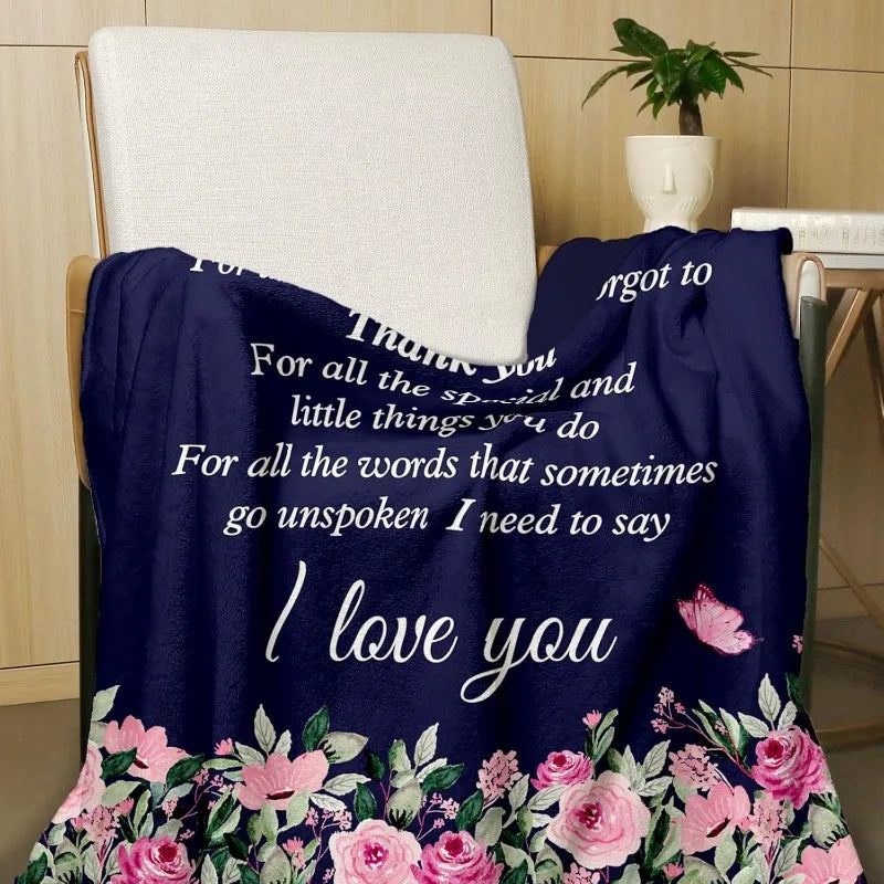 A dark blue throw blanket with pink floral embroidery is draped over a chair.