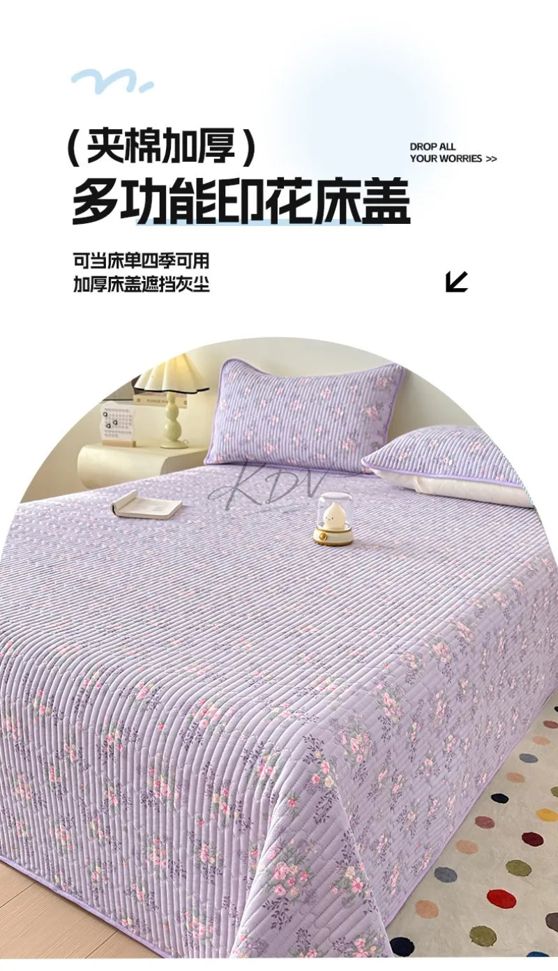 A purple floral quilted bedspread with pink and white flowers is displayed on a bed.