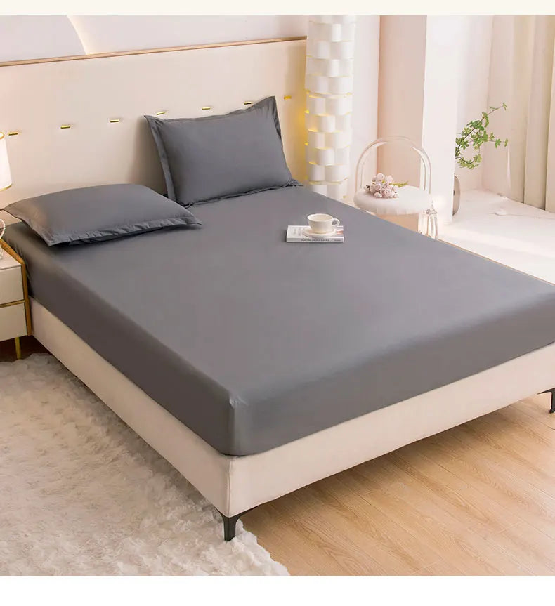 A gray waterproof fitted bed sheet set displayed on a modern bed with white linens and natural light.