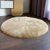 A round, light beige faux fur sheepskin area rug placed on a dark wood floor.