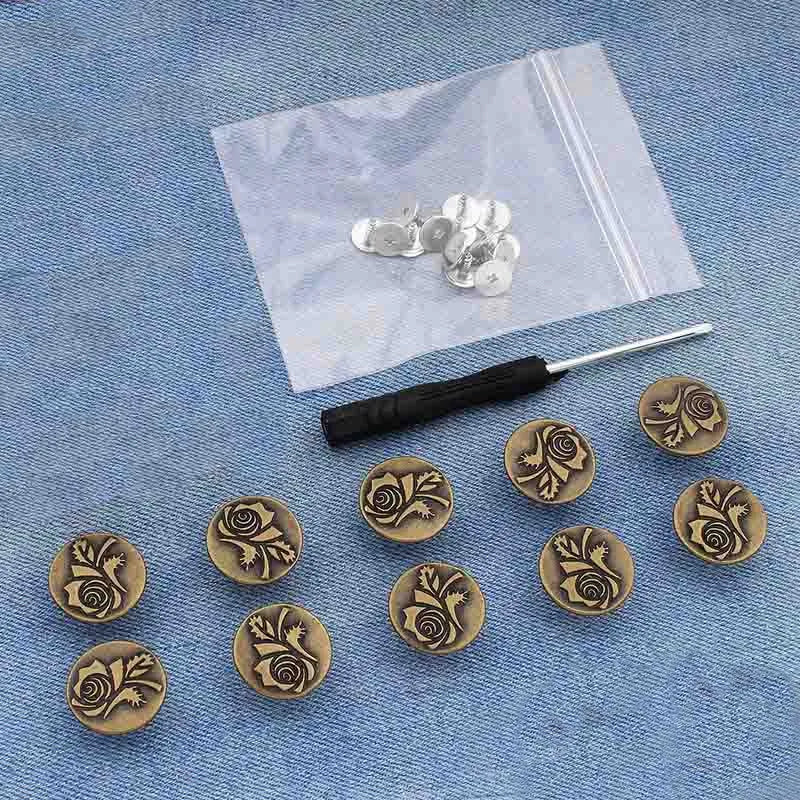 Silver metal button pins with floral designs are displayed on a white cloth against a blue fabric background.