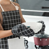 A person wearing a brown apron is holding a white bowl with black checkered oven gloves.