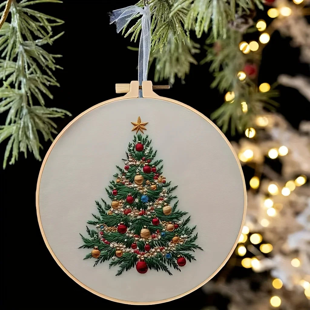 A round embroidery hoop featuring a detailed Christmas tree design with red and gold ornaments on a light background.
