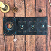 A dark fabric pouch decorated with celestial symbols and floral elements, resting on a wooden surface.