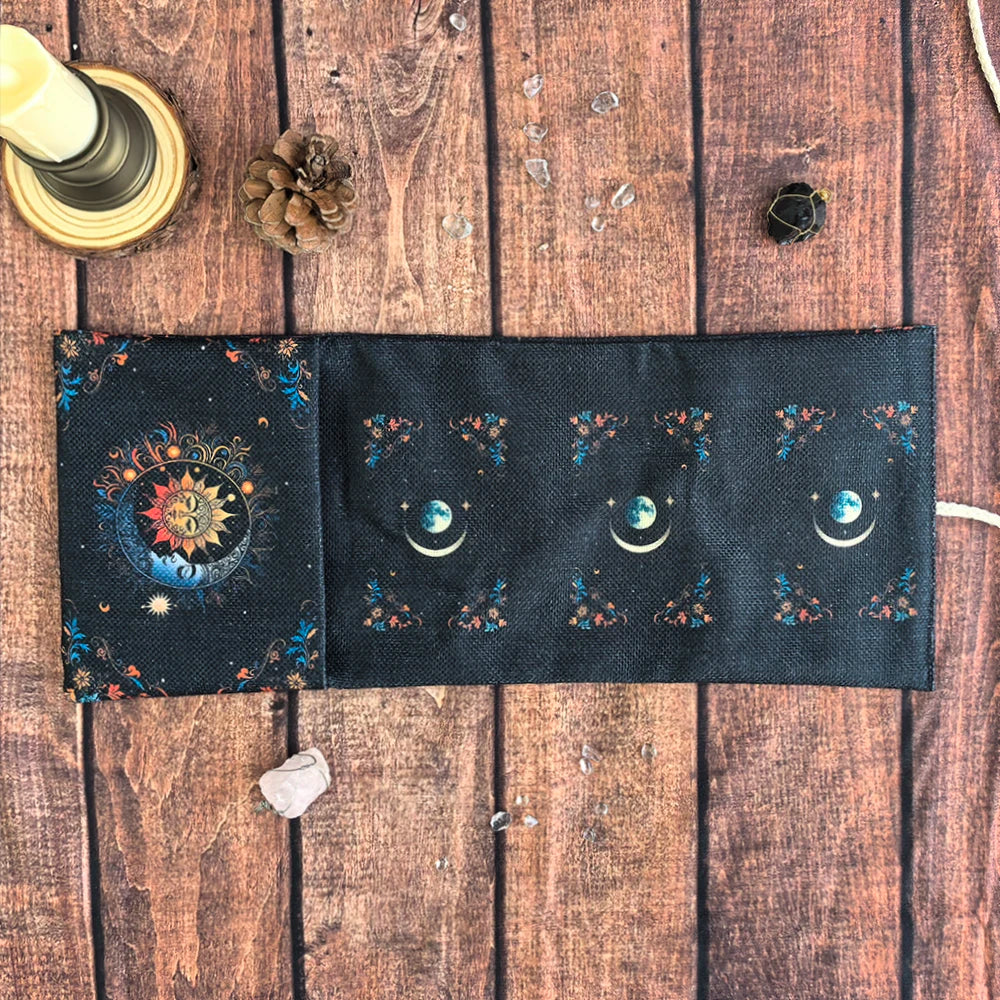 A dark fabric pouch decorated with celestial symbols and floral elements, resting on a wooden surface.