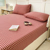 A red and white checkered fitted sheet is laid out on a bed with pillows and a clock nearby.