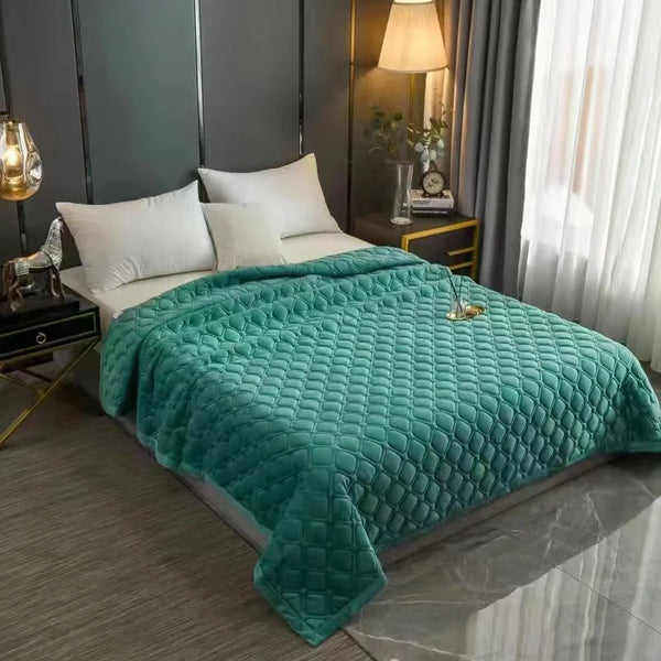A teal quilted velvet bed cover blanket spread on a bed with white pillows and dark gray curtains.