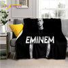 A black graphic throw blanket featuring a portrait of Eminem on a gray sofa.