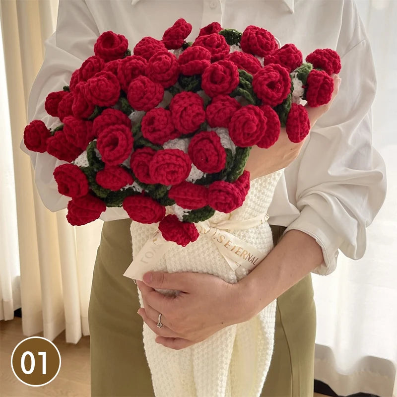 A hand knitted floral rose bouquet is held by a person, with a cream colored throw blanket visible.