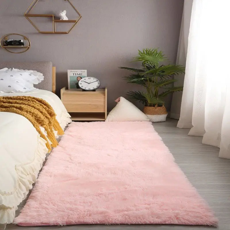 A pink fluffy rug is placed on a light gray floor next to a bed with white linens and wooden decor.