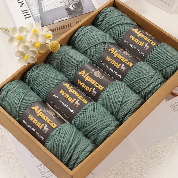 A box filled with various skeins of green alpaca wool knitting yarn and a white flower.