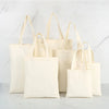 A collection of natural canvas tote bags in off-white and cream colors displayed on a white marble surface.